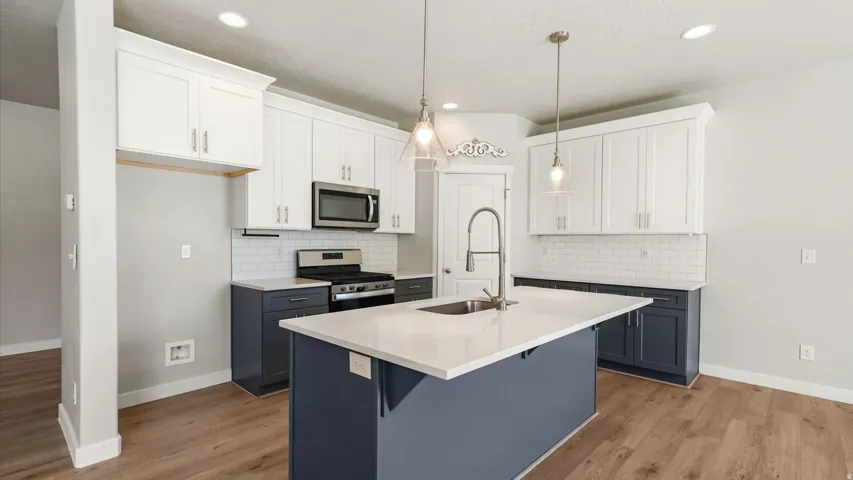 Modern kitchen featuring a large central island with a built-in sink, white countertops, and wood-finish flooring