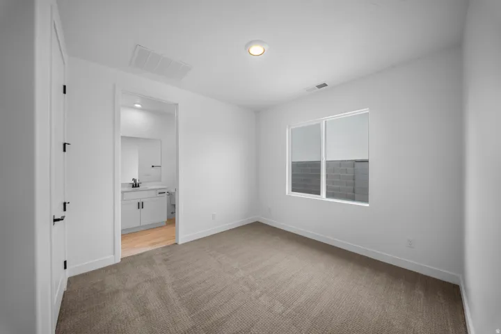 Casita Bright bedroom with neutral carpeting, a large window, and an en-suite bathroom featuring a vanity with a rectangular sink and wood-finish flooring
