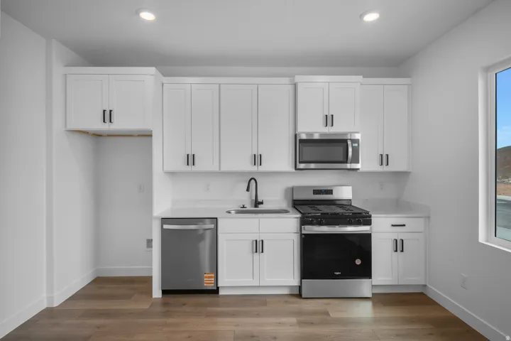 Casita Kitchen featuring white shaker cabinetry, stainless steel appliances, light-toned countertops, wood-finish flooring, and recessed lighting