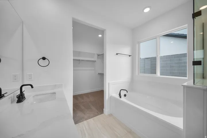 Contemporary bathroom featuring a spacious soaking tub, a single vanity with a white countertop and integrated sink, matte black fixtures, and light wood-finish flooring
