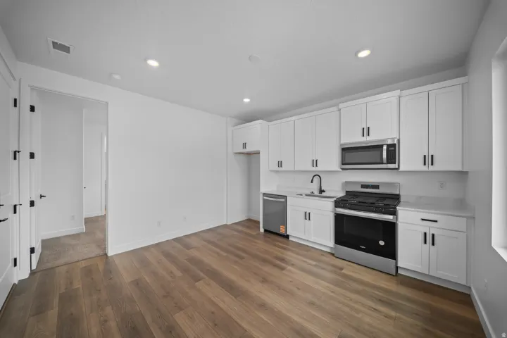 Casita kitchen featuring white shaker cabinetry, stainless steel appliances, a black faucet, light countertops, and wood-finish flooring