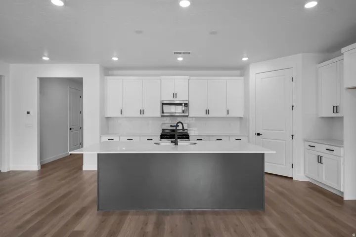 Modern kitchen featuring a dark gray island, white shaker-style cabinetry, and wood-finish flooring