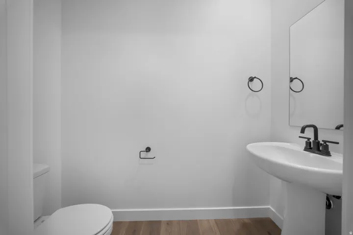 Pedestal sink with matte black faucet, wall-mounted mirror, and wood-finish flooring