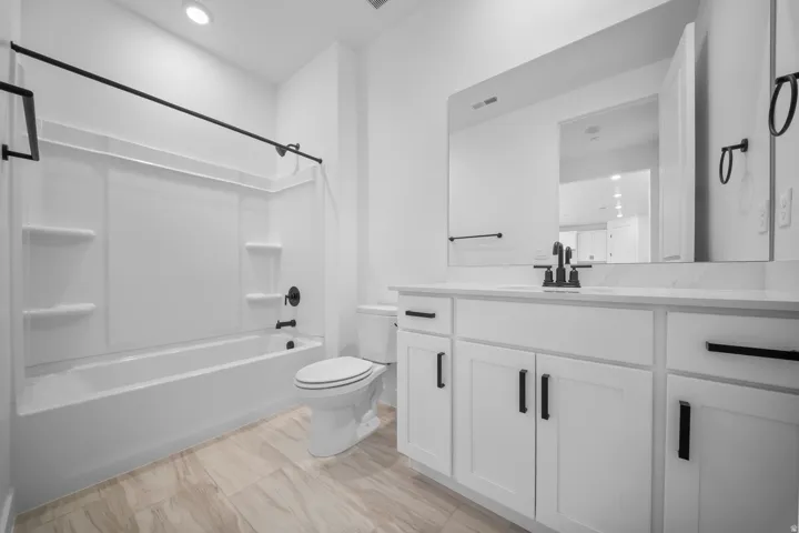 Full bathroom featuring a white tub/shower combination with matte black fixtures, a white vanity with slab countertop, and wood-finish flooring