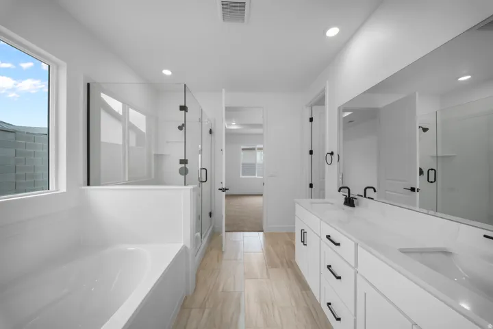 Spacious bathroom featuring a dual vanity with white cabinetry and undermount sinks, a large frameless mirror, a glass-enclosed shower, and a separate soaking tub