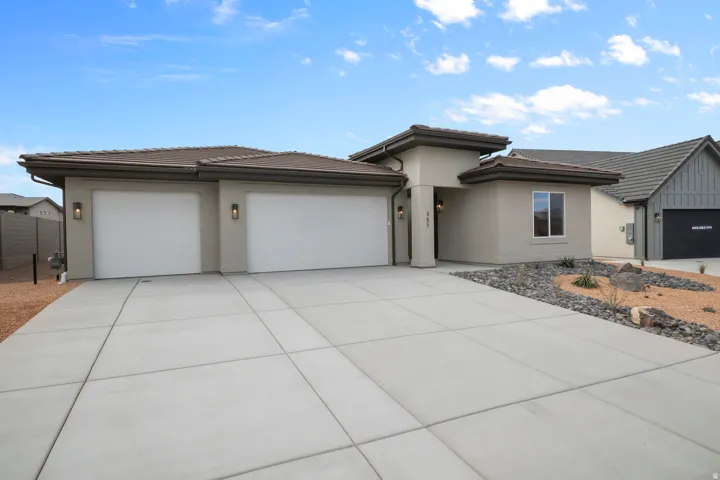 Contemporary stucco exterior featuring a two-car garage, concrete driveway, and xeriscaped front landscaping