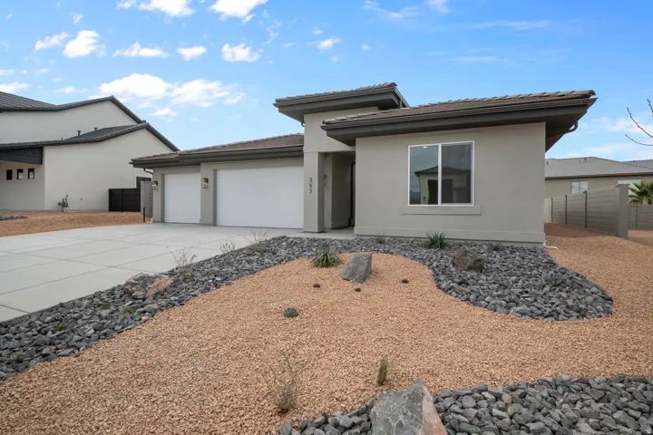 Contemporary stucco exterior featuring a two-car garage, concrete driveway, and desert-style landscaping with decorative rock and gravel