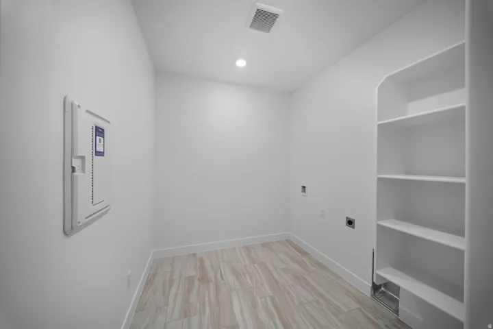 Dedicated utility area featuring wood-finish flooring, recessed lighting, built-in shelving, white baseboards, and a wall-mounted electrical panel