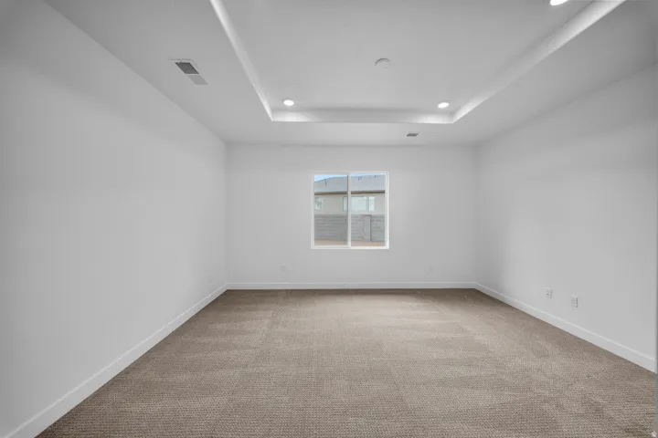 Spacious room featuring a tray ceiling with recessed lighting, plush carpet flooring, a large window, white baseboards, and neutral wall tones