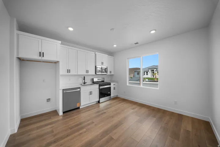 Kitchen area featuring white cabinetry, stainless steel appliances, wood-finish flooring, recessed lighting, and a double-pane window