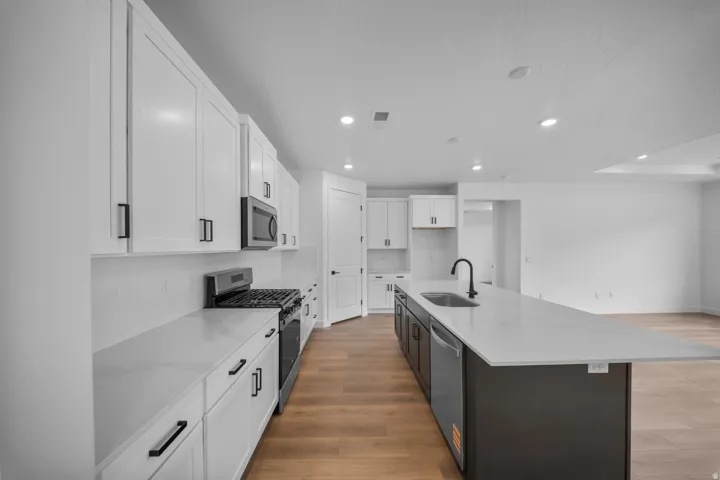 Contemporary kitchen featuring white cabinetry, quartz countertops, stainless steel appliances, and wood-finish flooring