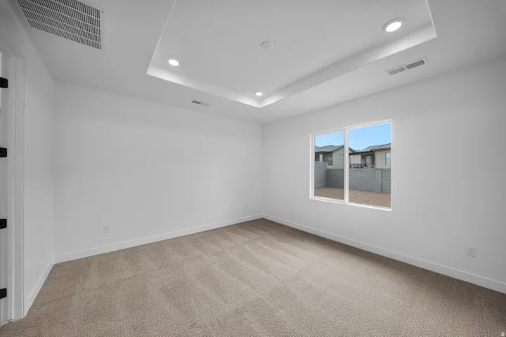 Recessed ceiling with integrated lighting, a large window, and light-toned carpeting