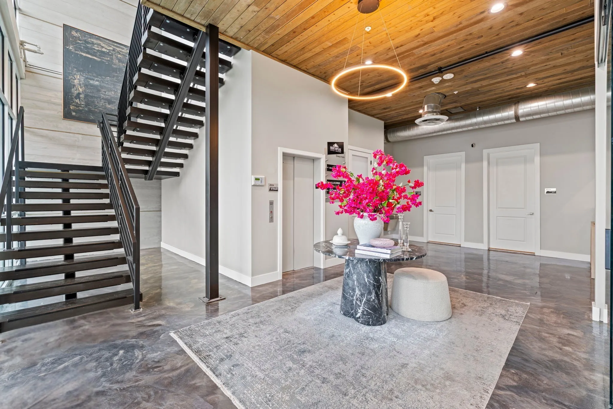Industrial-inspired open staircase with black metal railings and treads, polished concrete flooring, a wood-paneled ceiling, exposed ductwork, and a circular overhead light fixture