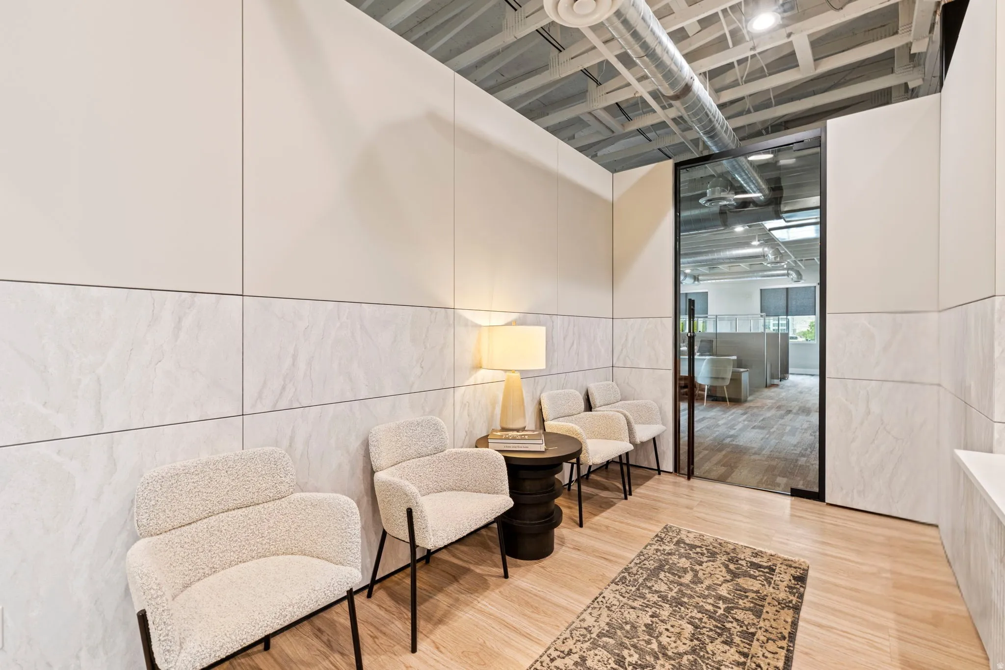Modern commercial waiting area featuring light wood-finish flooring, half-wall stone-look paneling, and an exposed ceiling with ductwork