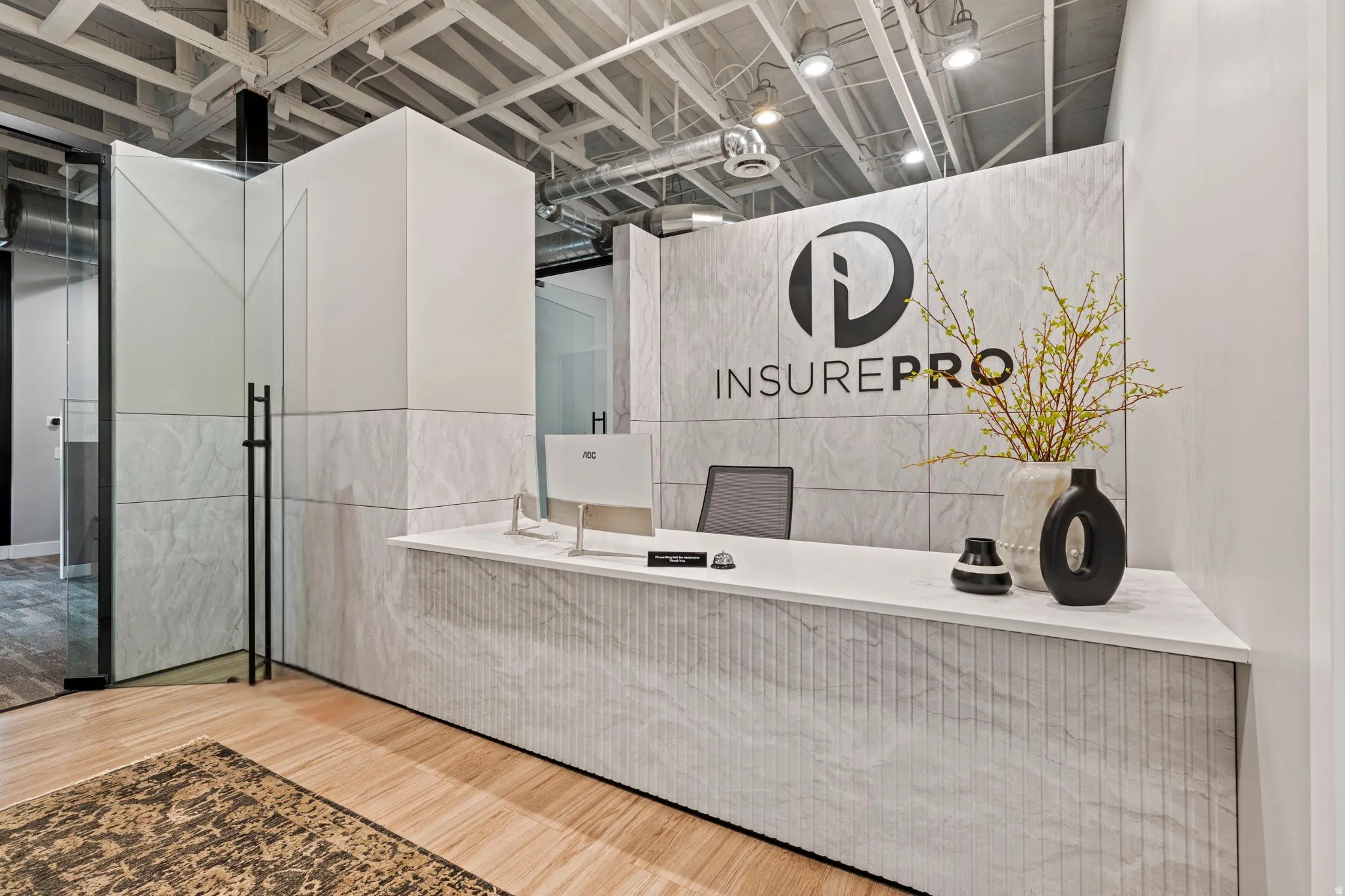 Reception area featuring a stone-finish desk with a fluted facade, complementary stone-finish accent wall, exposed ceiling with industrial lighting, glass partition, and wood-finish flooring