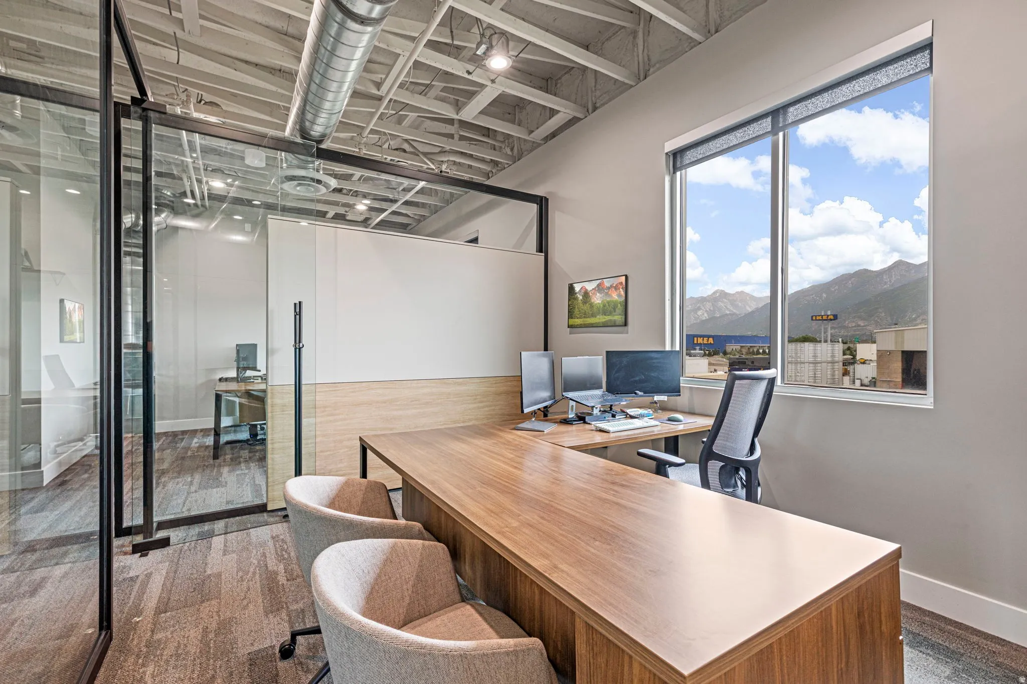 Private office space featuring a full-height window, exposed ductwork, wood-finish flooring, and a glass partition wall