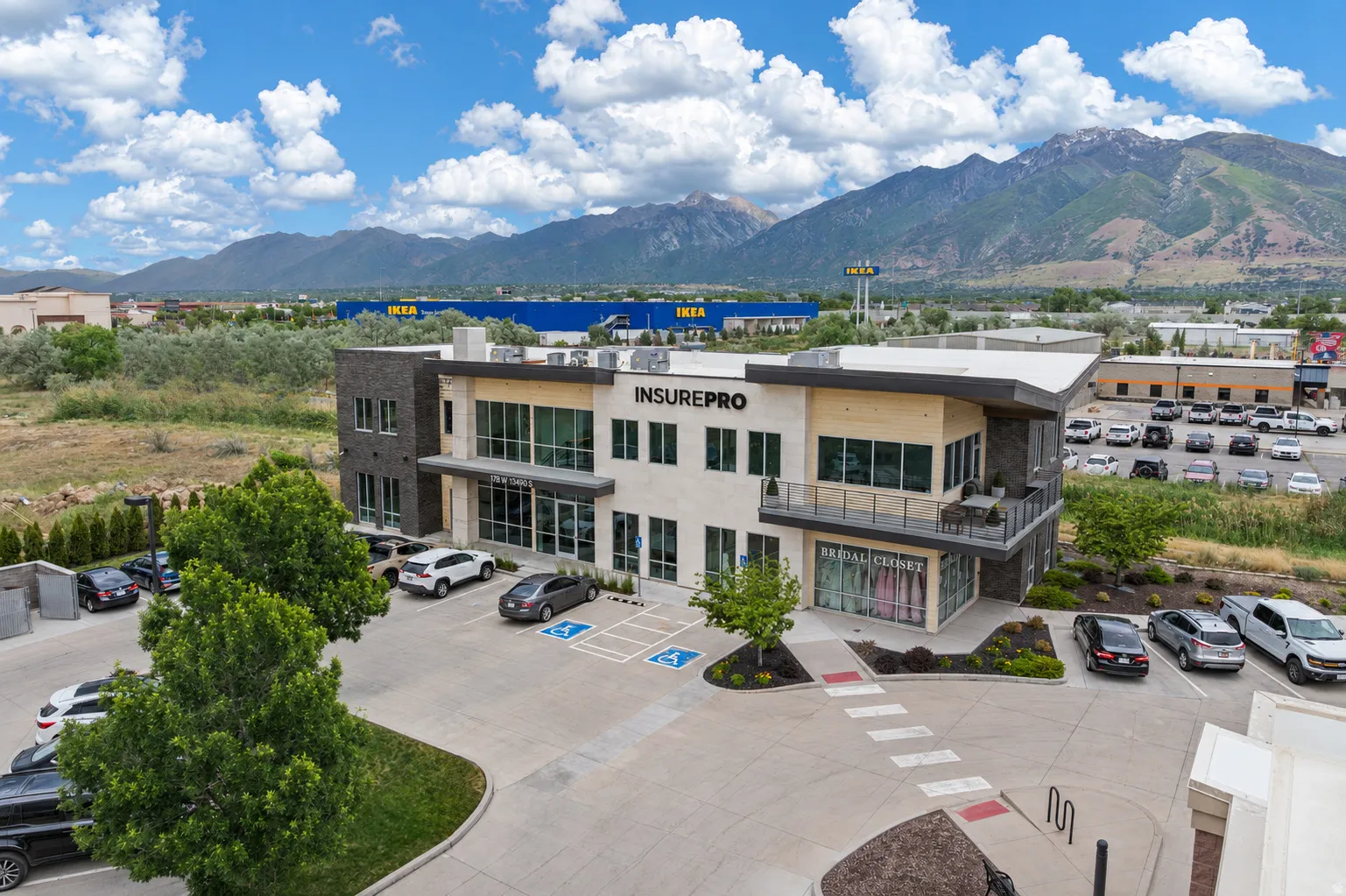 Modern commercial building featuring a stone and stucco exterior, prominent storefront windows, a second-story balcony, and dedicated parking spaces