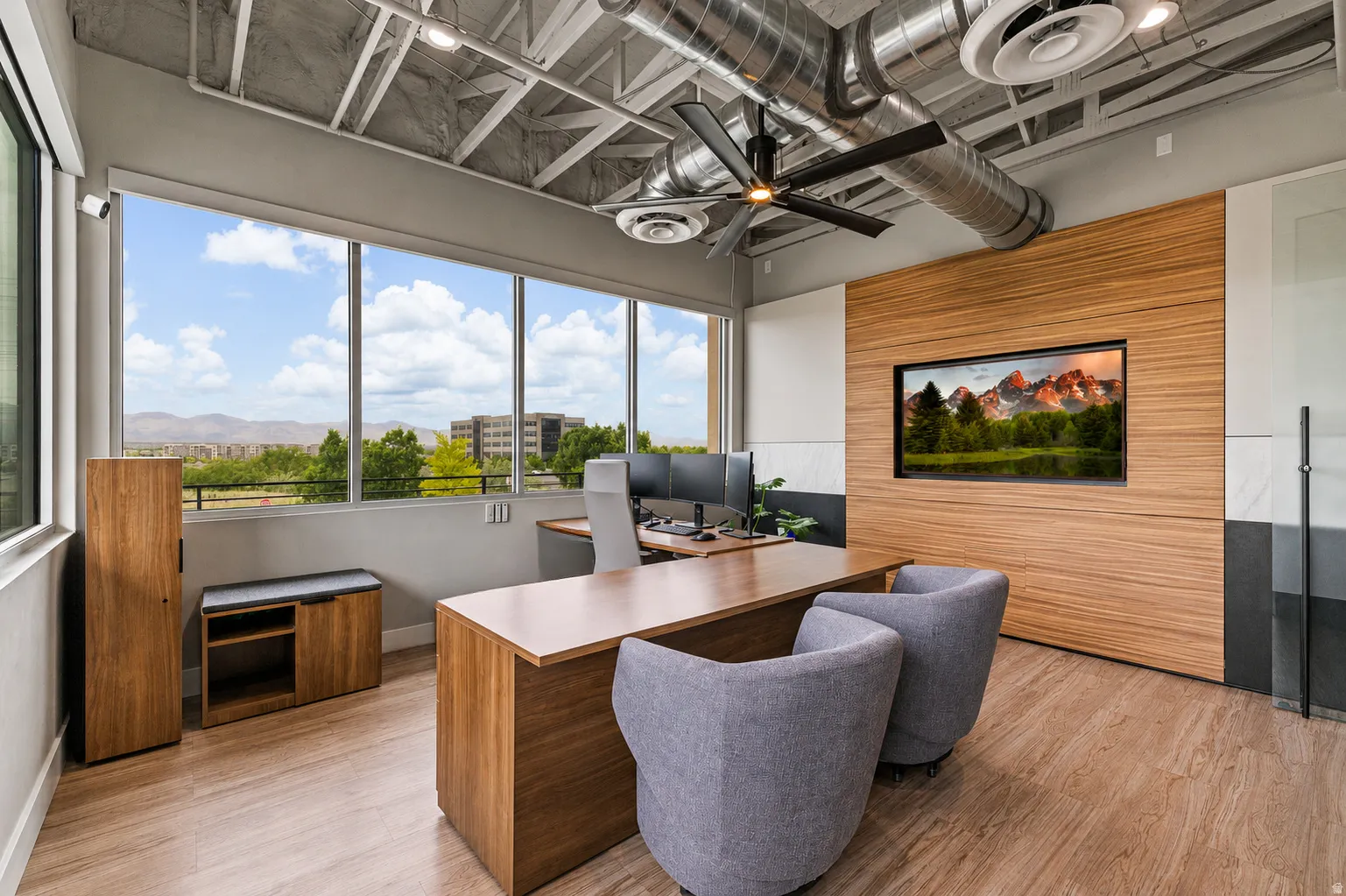 Expansive window wall with a mountain backdrop, exposed industrial-style ceiling, wood-finish flooring, and a built-in media display with wood paneling