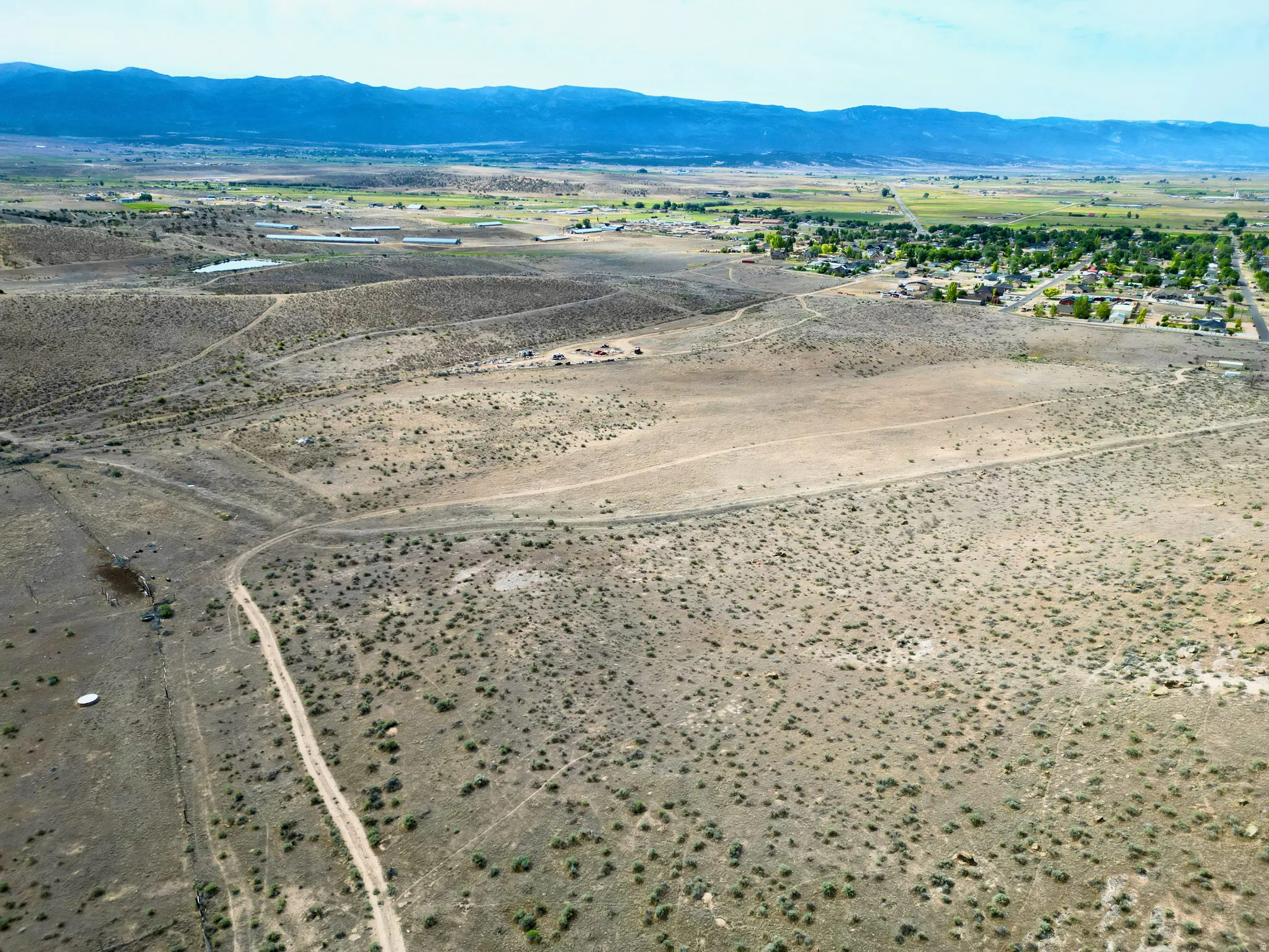 Expansive desert landscape featuring scattered brush, visible dirt paths, and distant mountain ranges