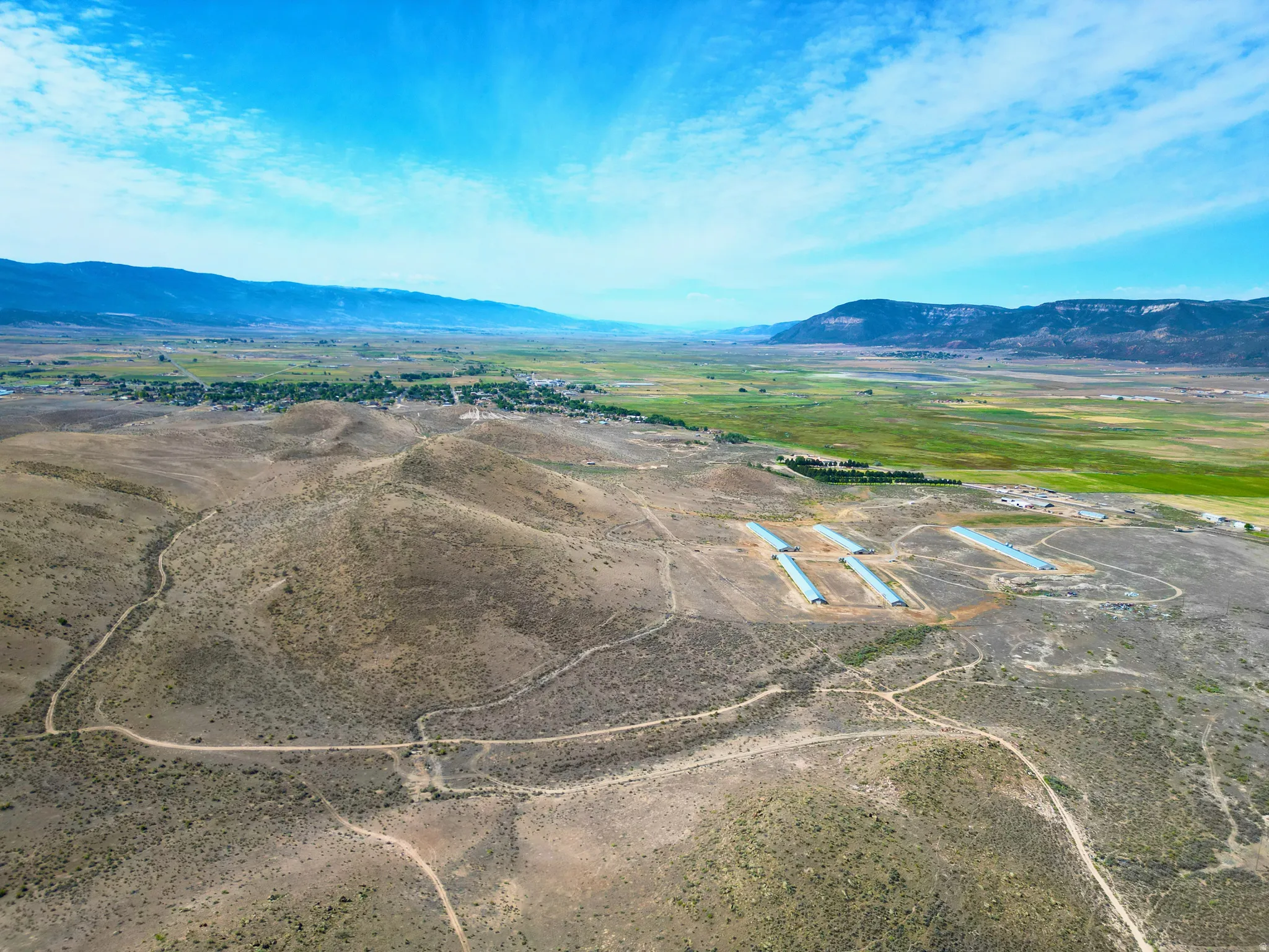 Expansive rural land featuring multiple agricultural structures, a network of unpaved roads, and distant mountainous terrain