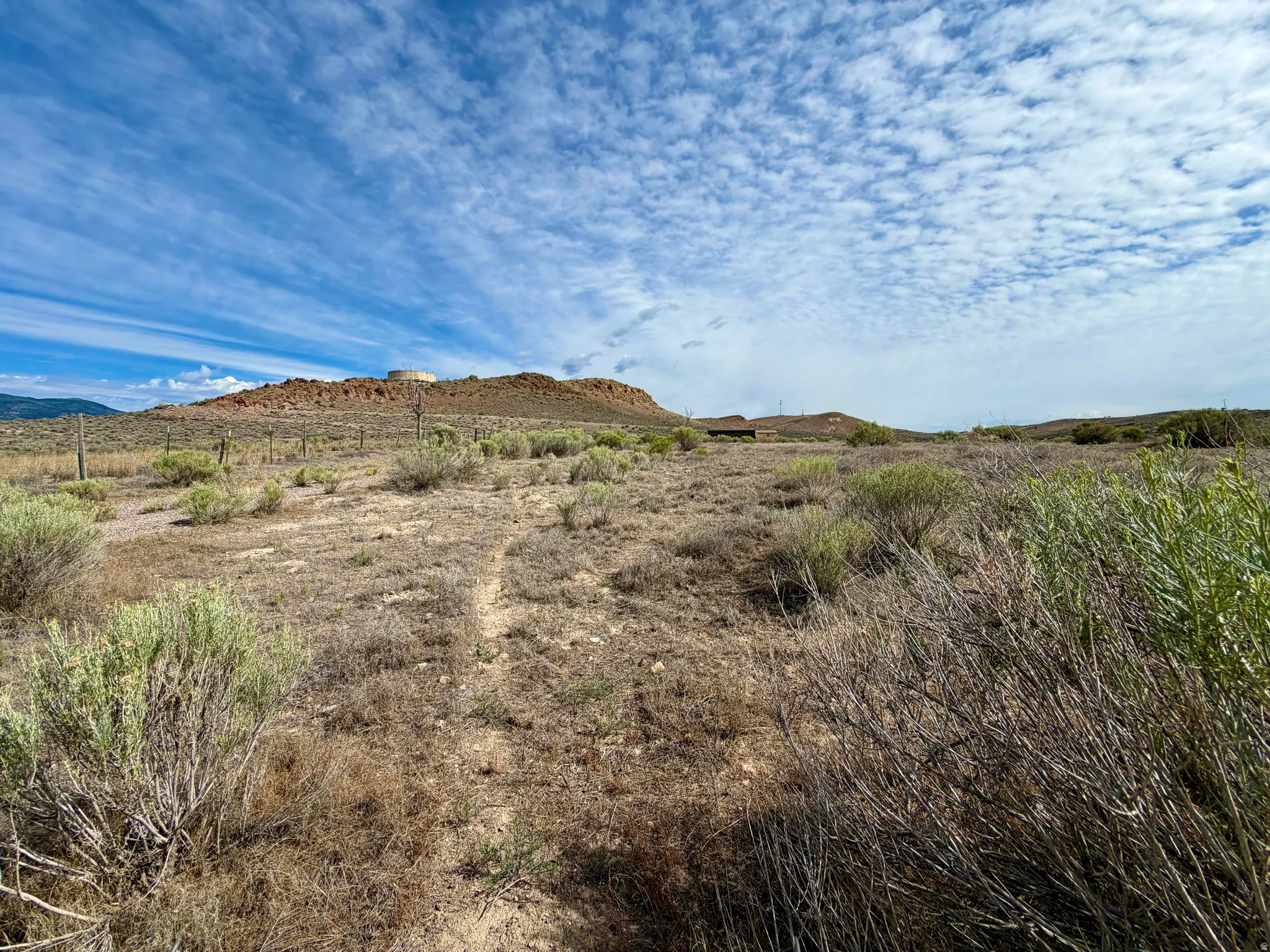Expansive land parcel featuring natural desert vegetation, a visible dirt path, and distant rocky hills under a broad sky