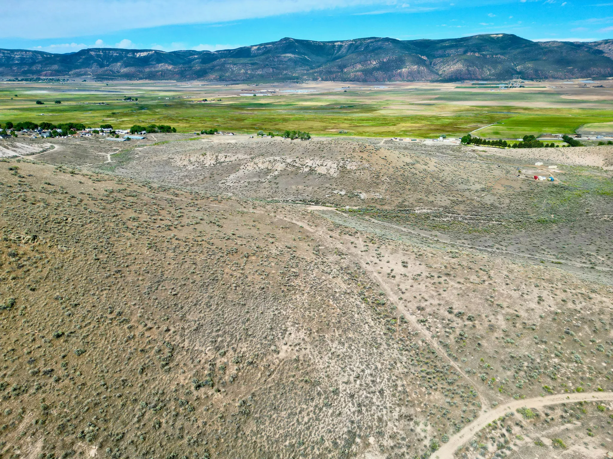Expansive rural landscape featuring distant mountains, a green valley, and an unpaved road