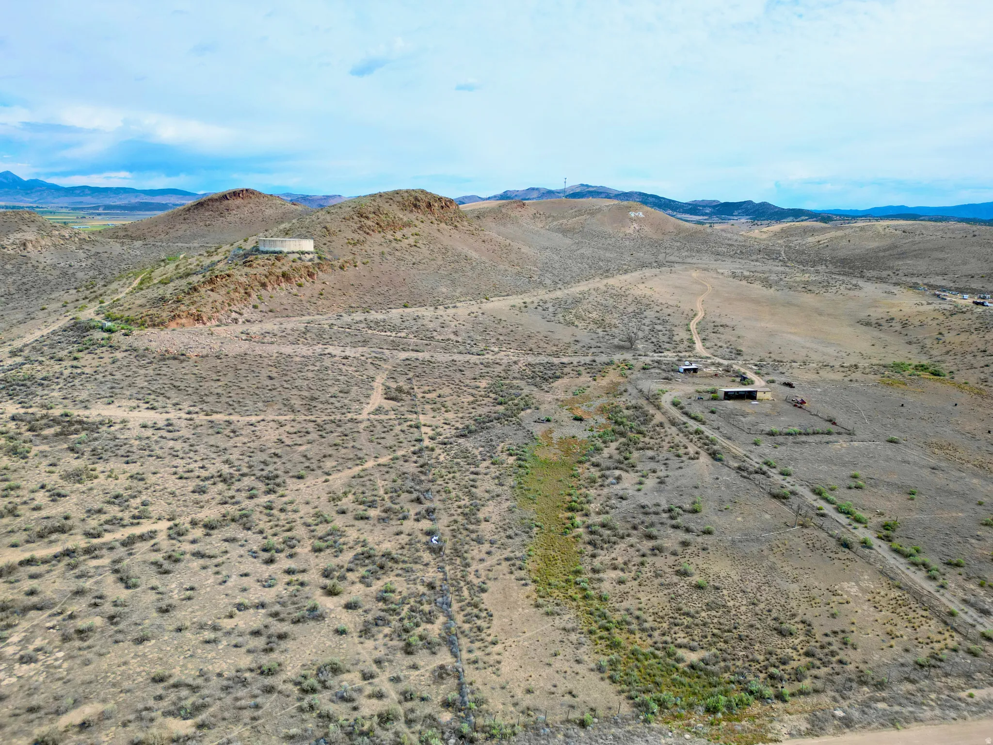 Expansive desert landscape featuring rolling hills, scattered brush, and unpaved pathways