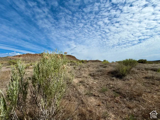 Expansive undeveloped land featuring natural desert vegetation, distant elevated terrain, and a broad sky with varied cloud formations