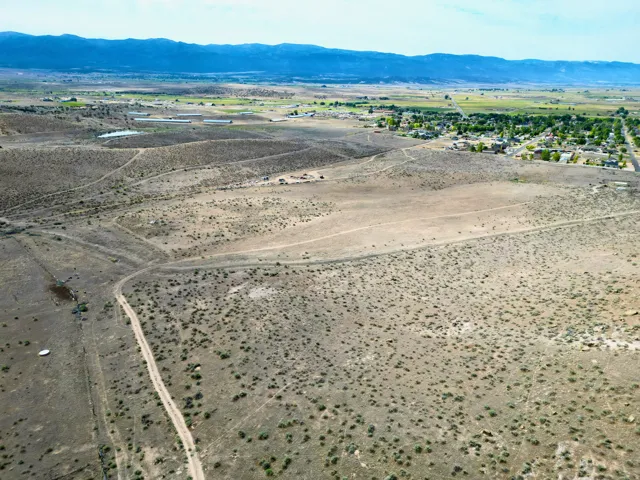 Expansive desert landscape featuring scattered brush, visible dirt paths, and distant mountain ranges