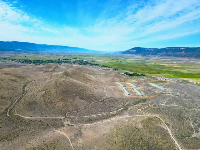Expansive rural land featuring multiple agricultural structures, a network of unpaved roads, and distant mountainous terrain