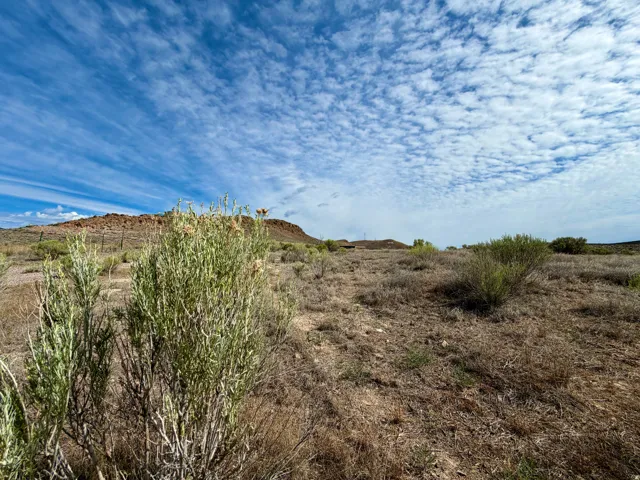 Expansive undeveloped land featuring natural desert vegetation, distant elevated terrain, and a broad sky with varied cloud formations