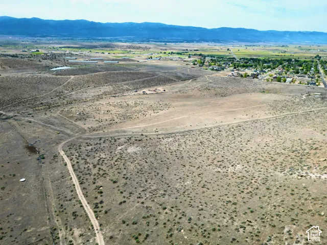Expansive desert landscape featuring scattered brush, visible dirt paths, and distant mountain ranges