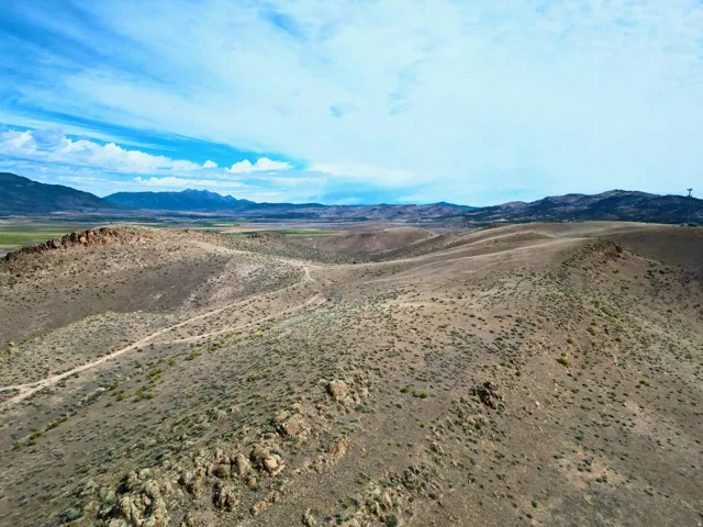 Expansive undeveloped land featuring rolling hills, natural rock formations, sparse vegetation, and distant mountain ranges