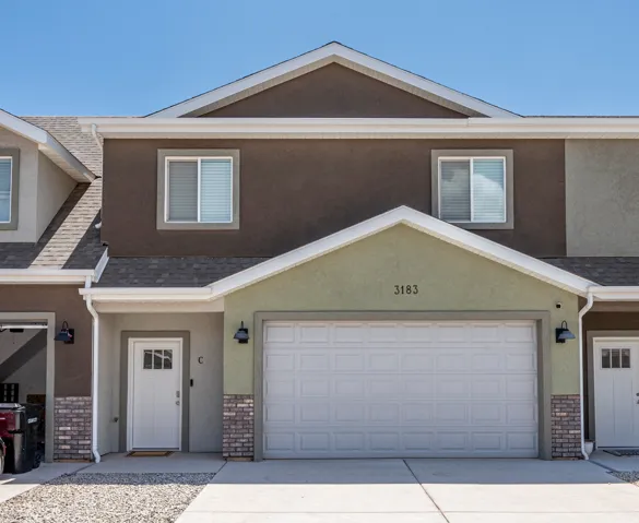 Multi-story exterior featuring a single-panel garage door, a white entry door with glass inserts, and contrasting stucco siding