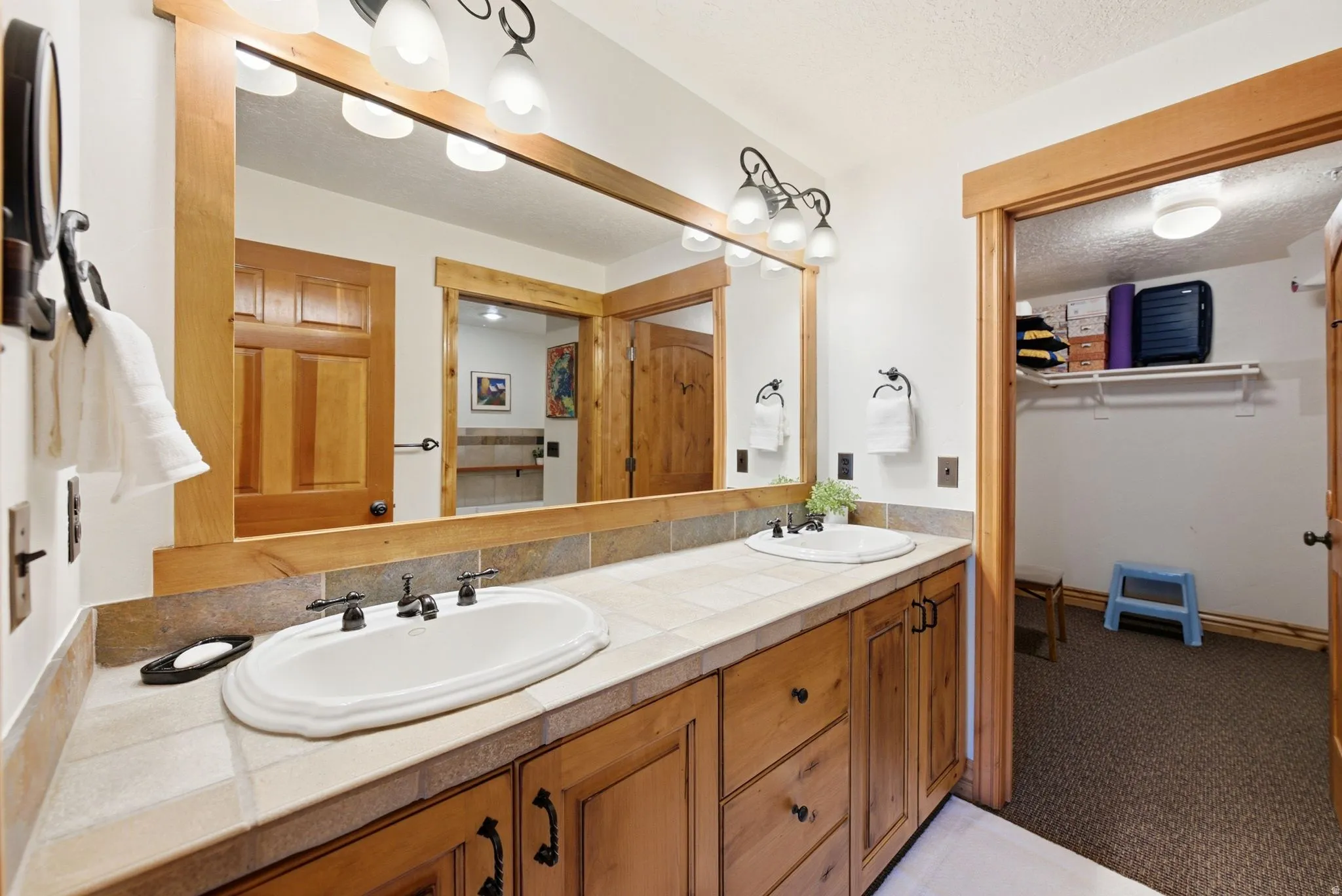 Double vanity featuring oval undermount sinks, tile countertops, and rich wood cabinetry