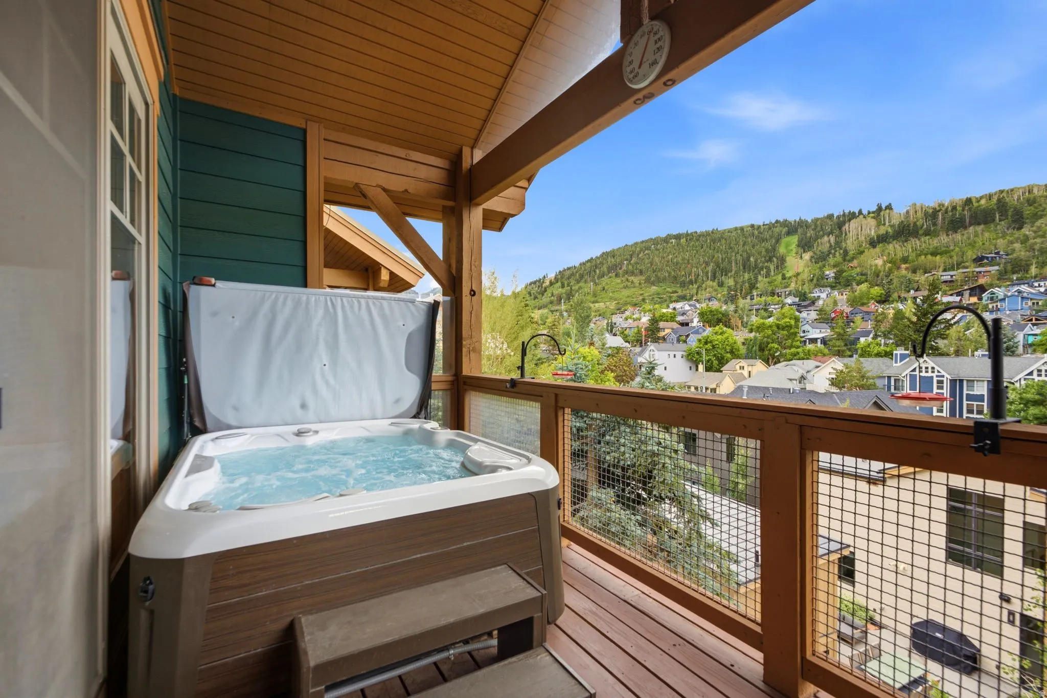 Covered balcony featuring a built-in hot tub with a raised cover, wood-finish flooring, and a mesh-paneled railing