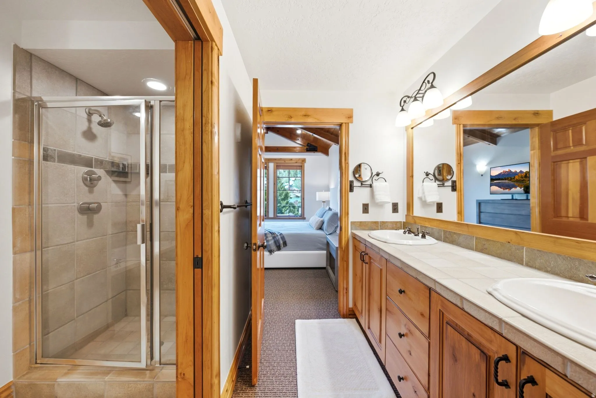 Bathroom featuring a dual vanity with wood cabinetry, tile countertops, and a large mirror