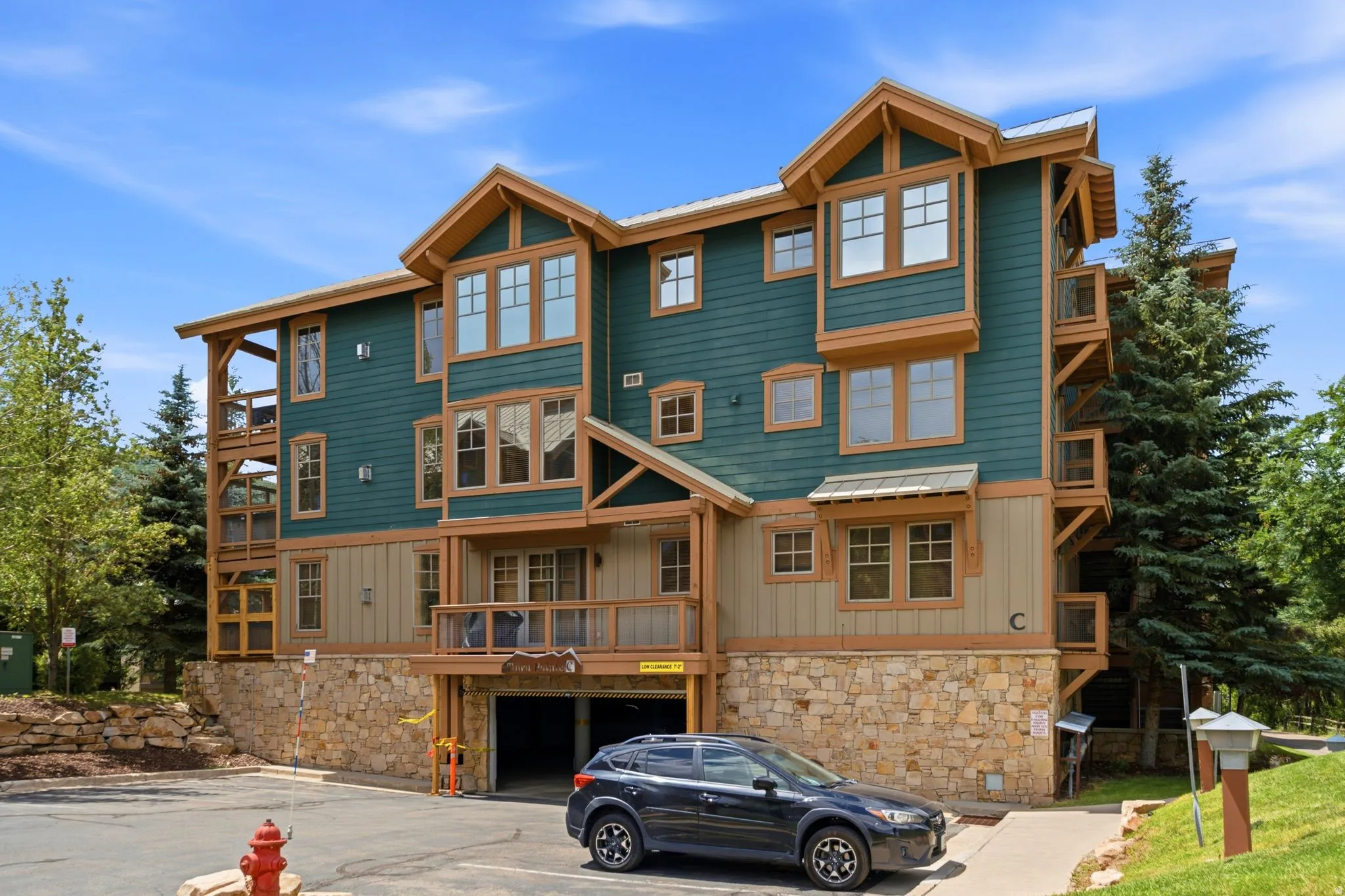 Multi-story property featuring a stone and siding exterior, multiple balconies, an integrated garage, and surrounding mature trees