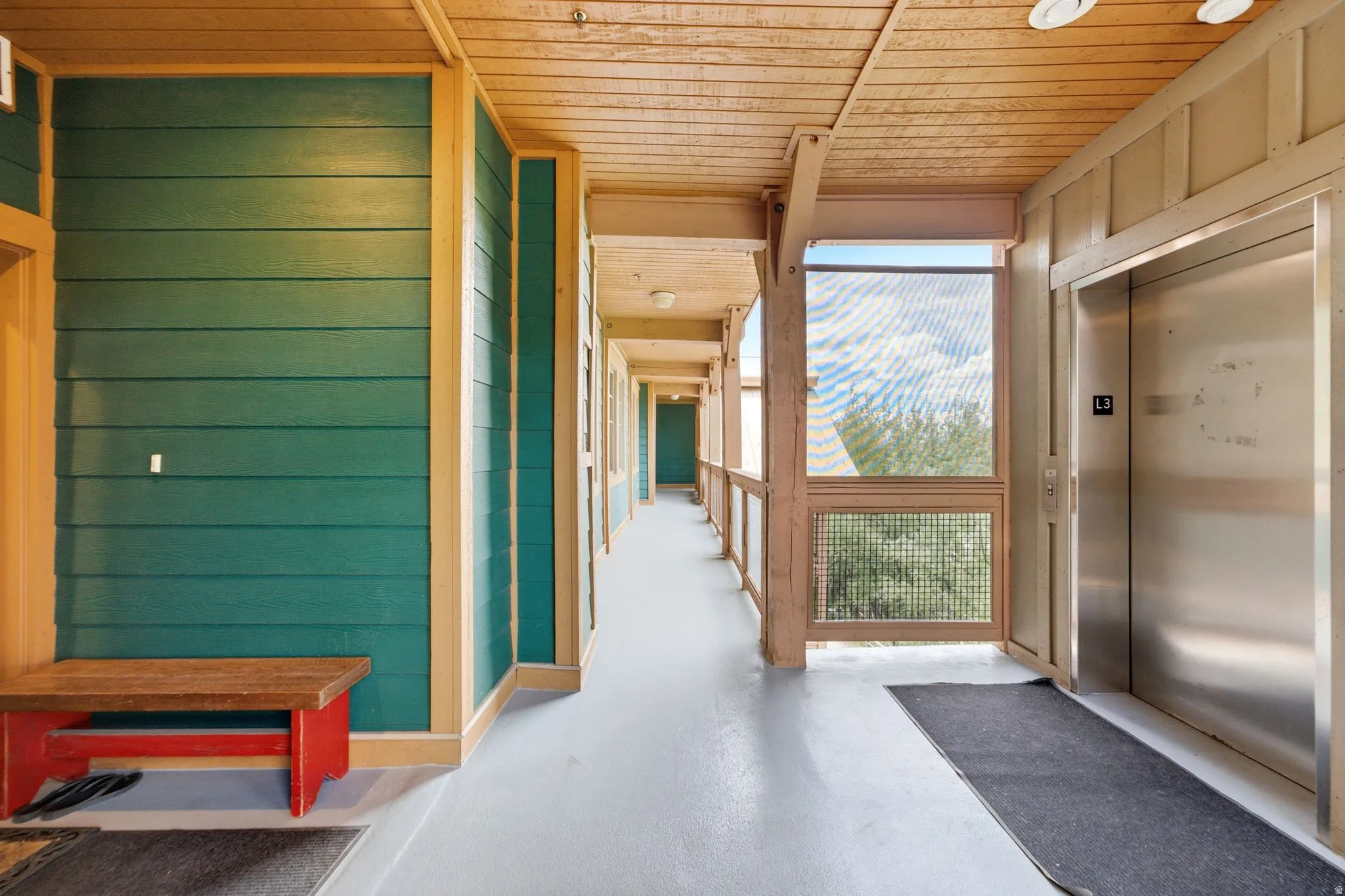 Outdoor hallway featuring wood-finish ceiling, light gray flooring, and green plank siding