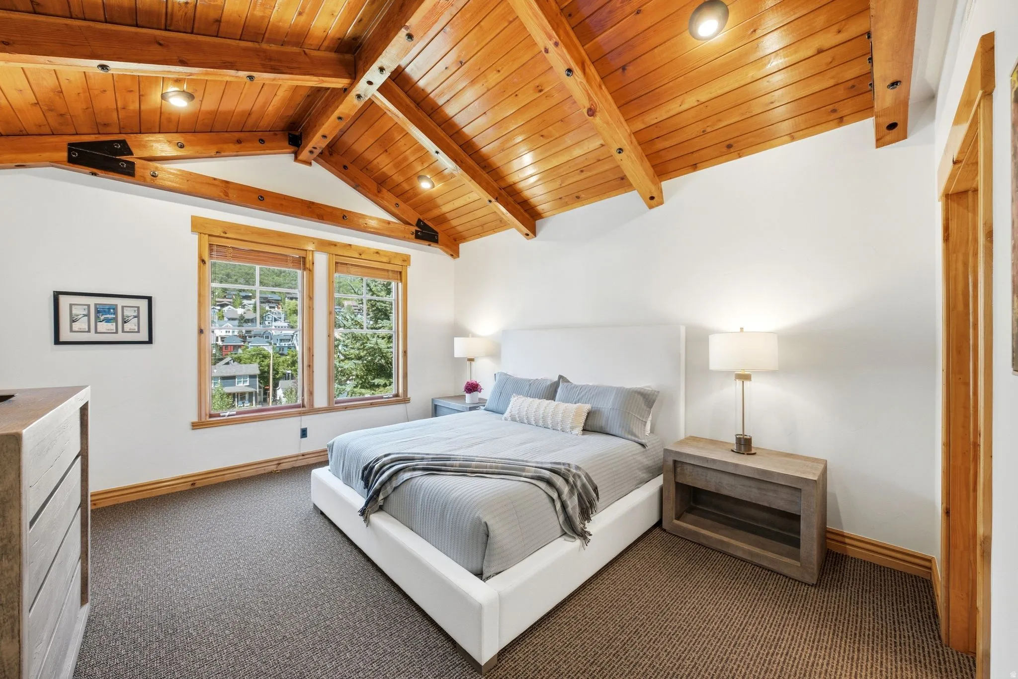 Vaulted wood-paneled ceiling with exposed beams, dual windows, wood-trimmed doorway, and textured carpeting