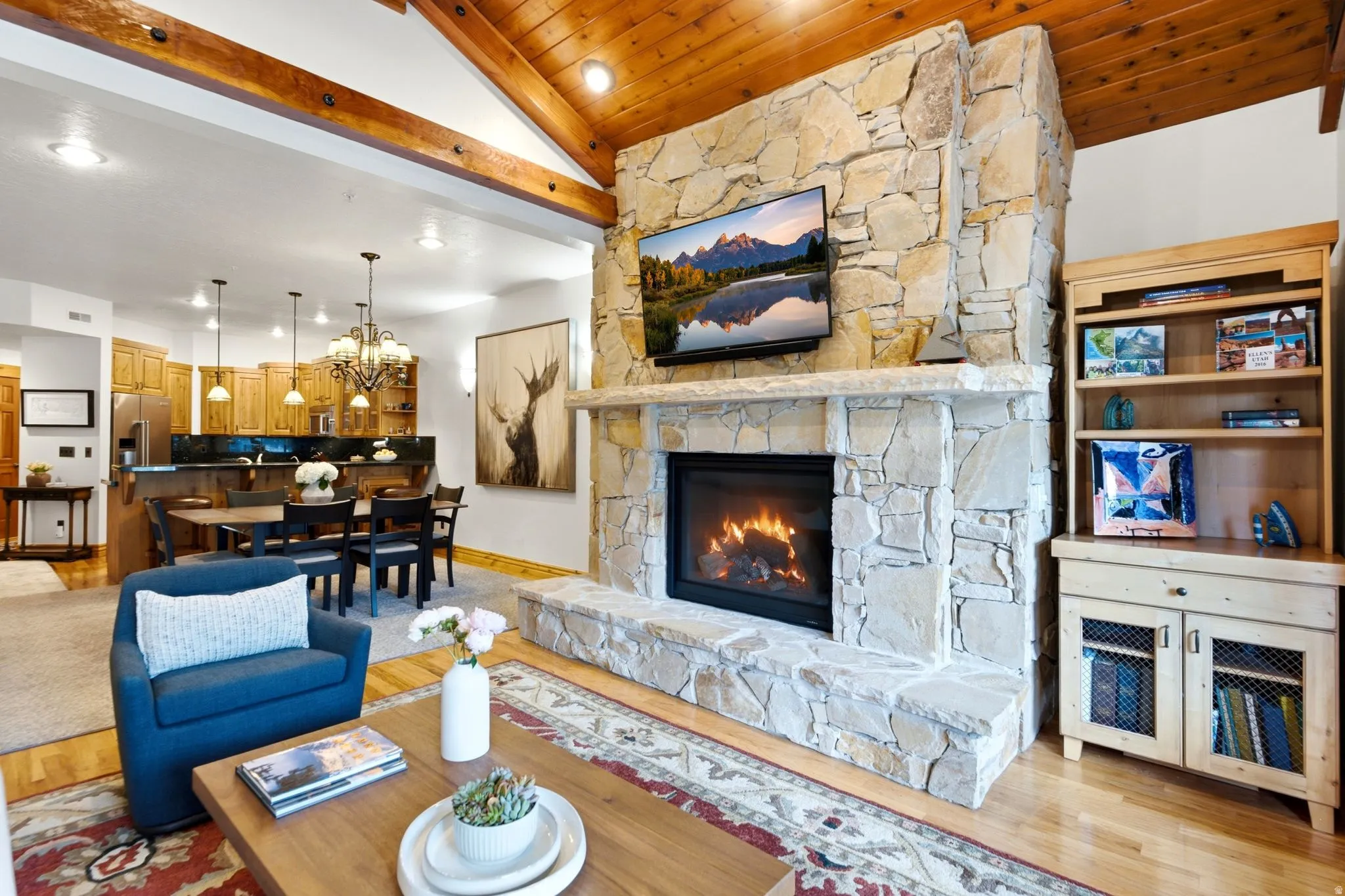 Stone fireplace with a hearth, wood-finish flooring, vaulted wood-paneled ceiling with exposed beams, recessed lighting, and built-in shelving