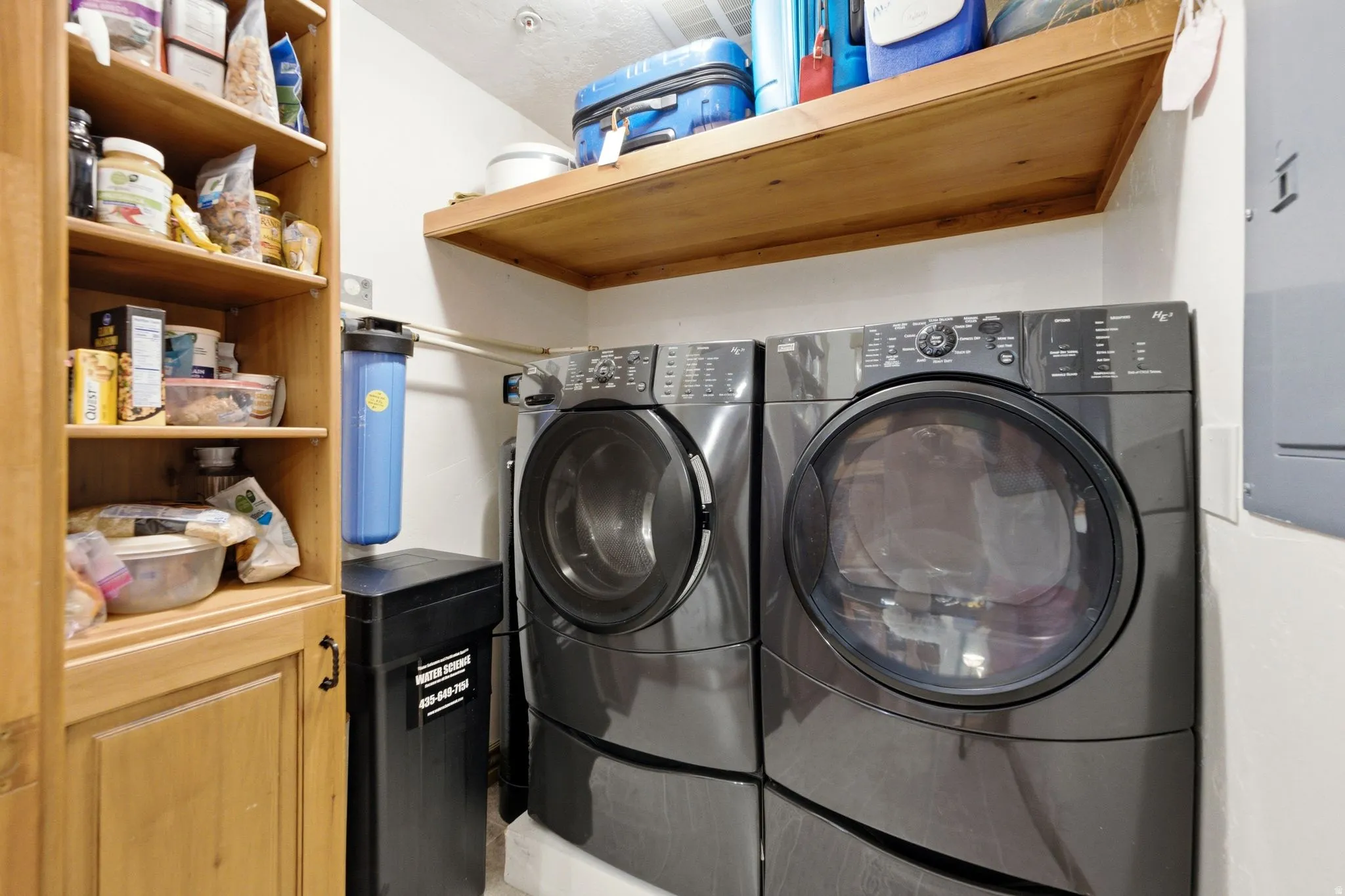 Dedicated laundry area featuring front-loading washer and dryer, built-in shelving, wood-finish cabinetry, and a water filtration system