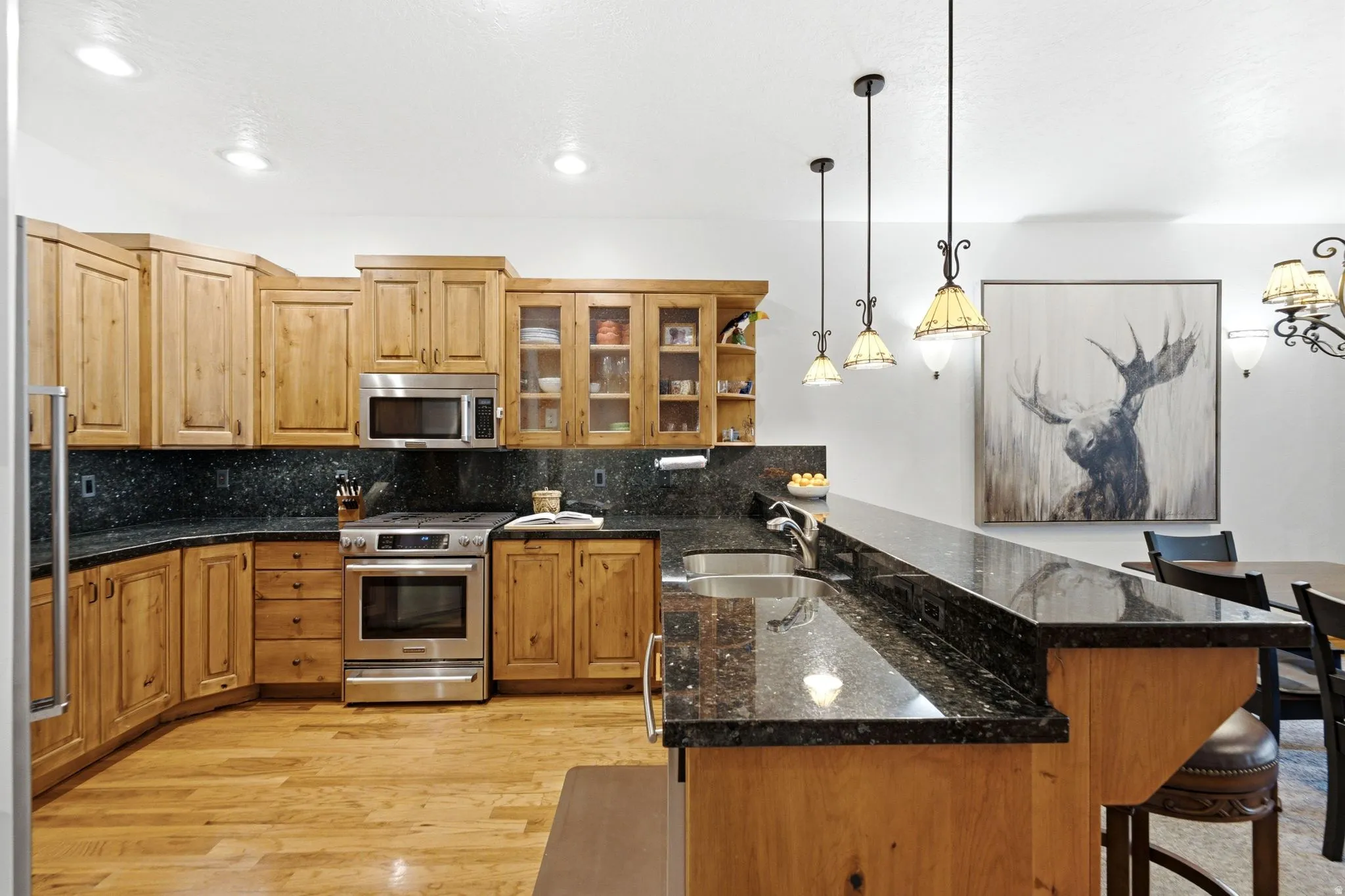 Kitchen featuring light wood cabinetry, dark speckled countertops, stainless steel appliances, and wood-finish flooring