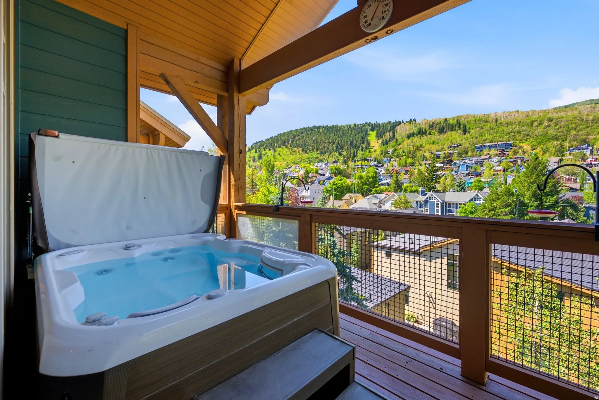 Covered outdoor deck with built-in hot tub, wood flooring, and metal railing