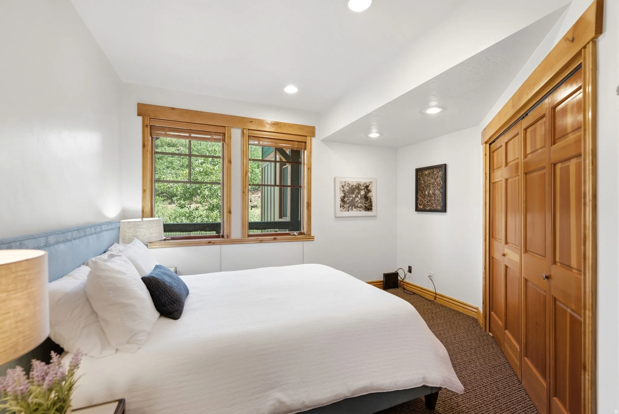 Bedroom featuring a pair of windows with natural wood trim, recessed lighting, carpet flooring, and bi-fold closet doors with natural wood panels