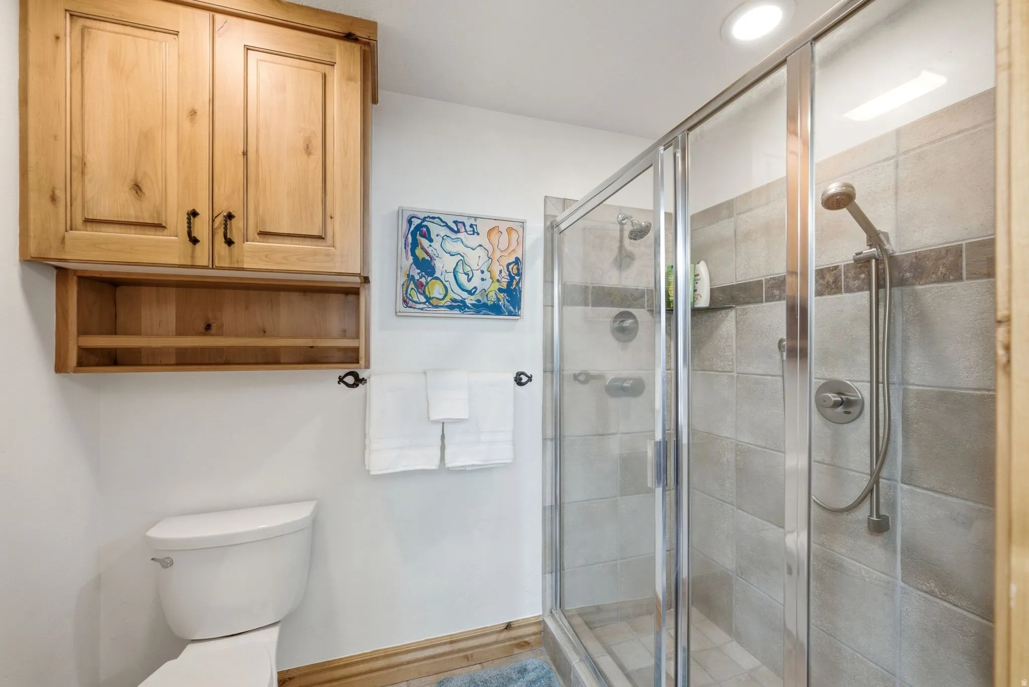 Glass-enclosed shower with a tiled surround, featuring a fixed showerhead and handheld sprayer