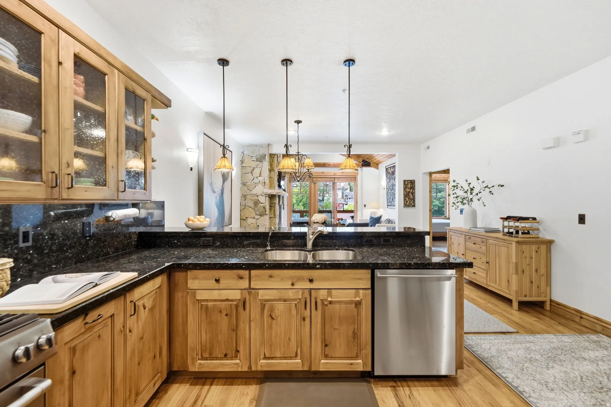 Kitchen featuring natural wood cabinetry with glass-front upper cabinets, dark speckled countertops, and a stainless steel dishwasher