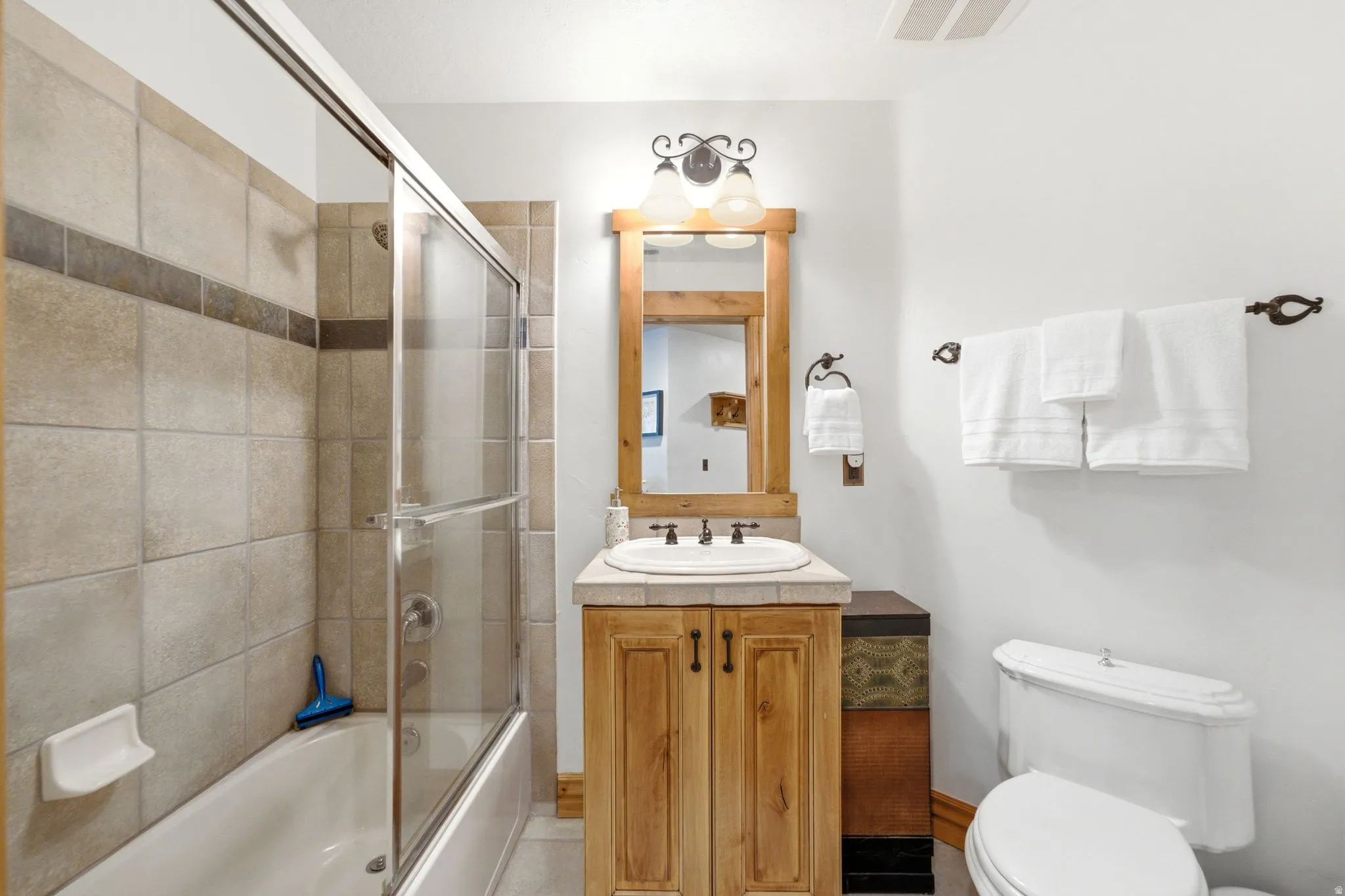 Bathroom featuring a light wood-finish vanity with a drop-in sink and a light-toned countertop
