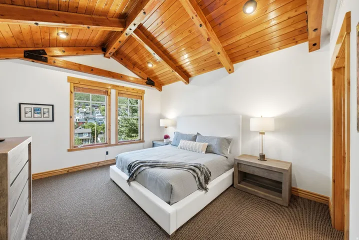 Vaulted wood-paneled ceiling with exposed beams, dual windows, wood-trimmed doorway, and textured carpeting