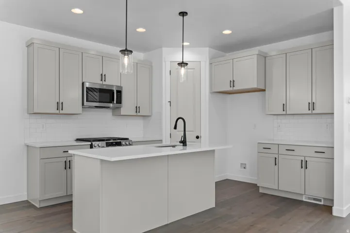 Modern kitchen showcasing light gray cabinetry, white subway tile backsplash, and wood-finish flooring